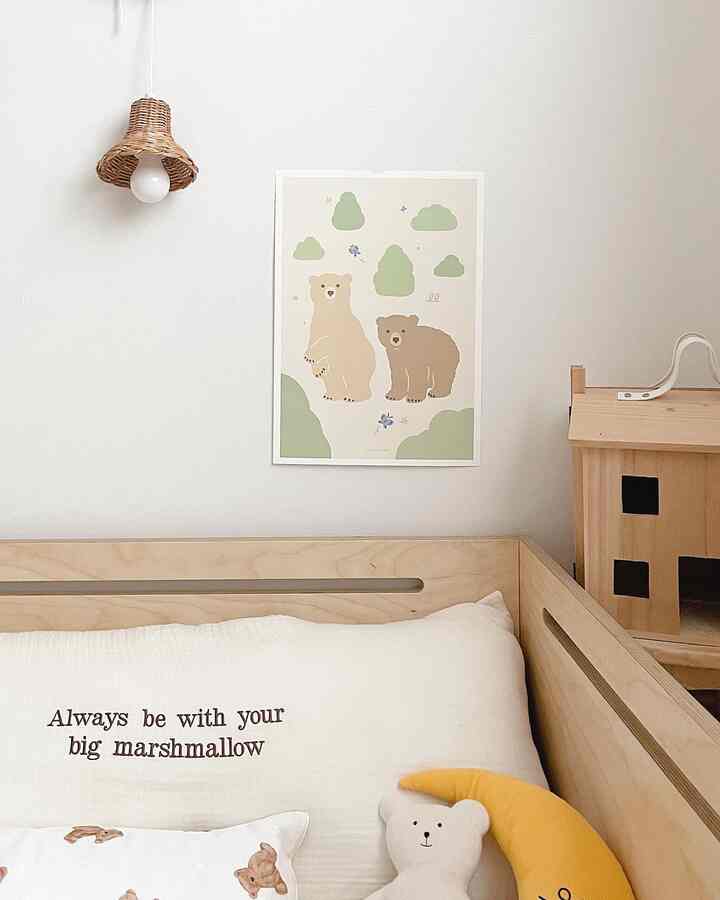 明るい白とベージュのナチュラルカラーの子供部屋、木製ベッドフレームとかわいいクマのポスター、月のクッションが配置された雰囲気のあるインテリア