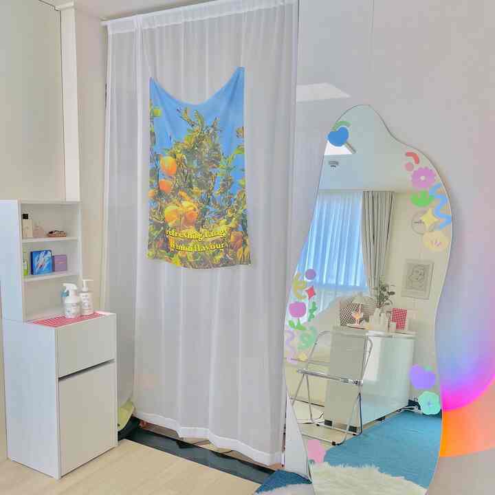 White-toned entrance space featuring an irregular shaped mirror, transparent folding chair, and a lemon-themed fabric curtain with a cozy and bright vibe