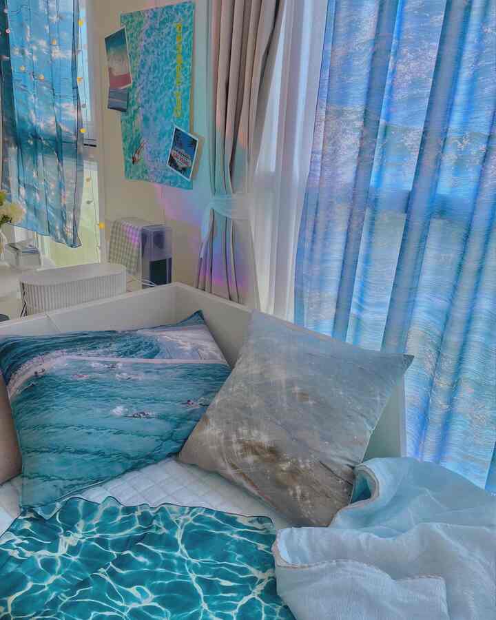 Blue-toned bedroom featuring ocean pattern curtains, pillows, and photo cushions creating a cool summer atmosphere