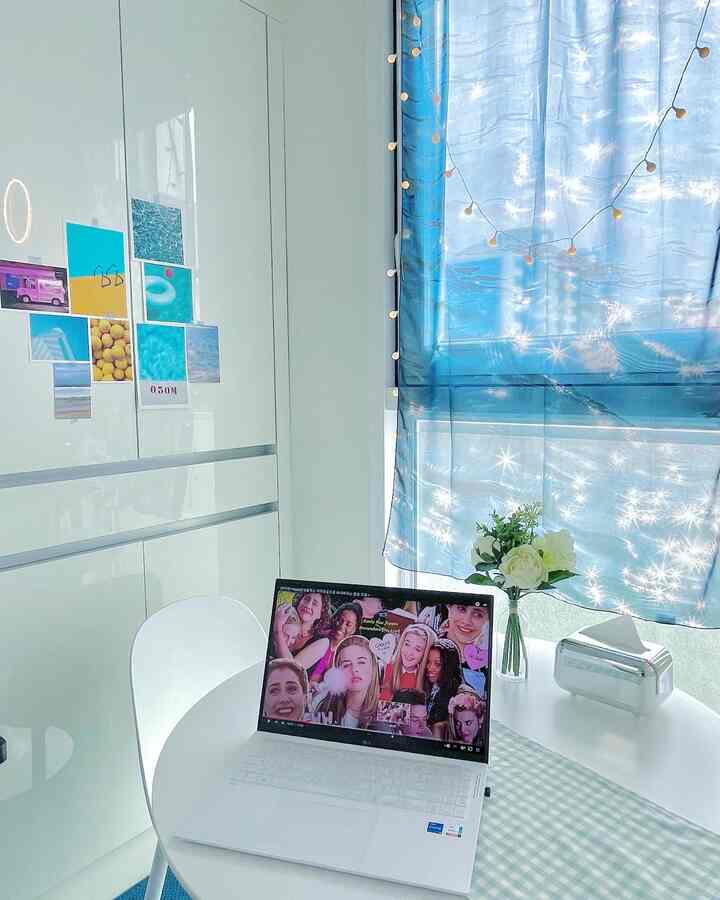 Bright studio apartment with white background, featuring blue curtains, posters, and a simple home office setup