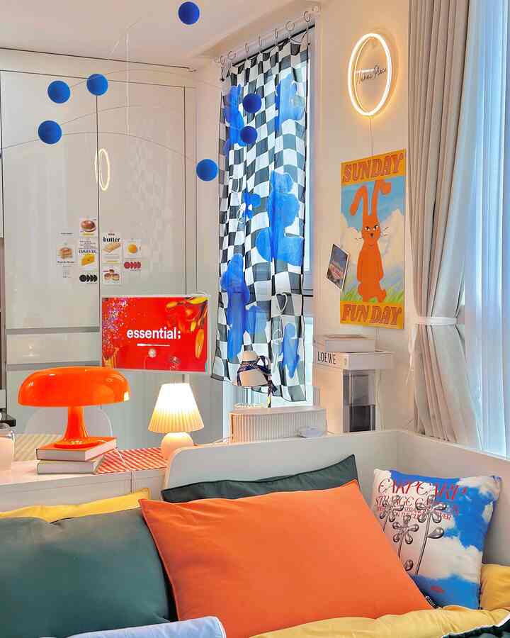 A white and orange-toned studio living room featuring varied lighting and fabric art with a modern atmosphere