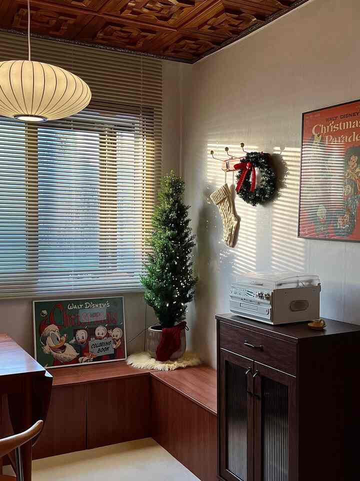 木目調と白いブラインドが調和するリビングの一角、細いクリスマスツリーとクリスマス飾りが特徴の温かみのあるインテリア