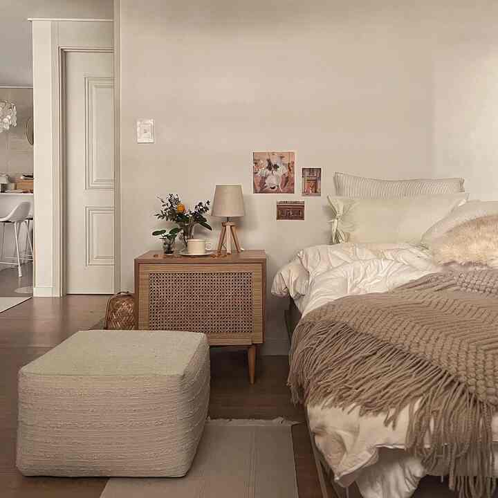 Beige and white toned bedroom featuring rattan nightstand and soft bedding with a cozy natural atmosphere