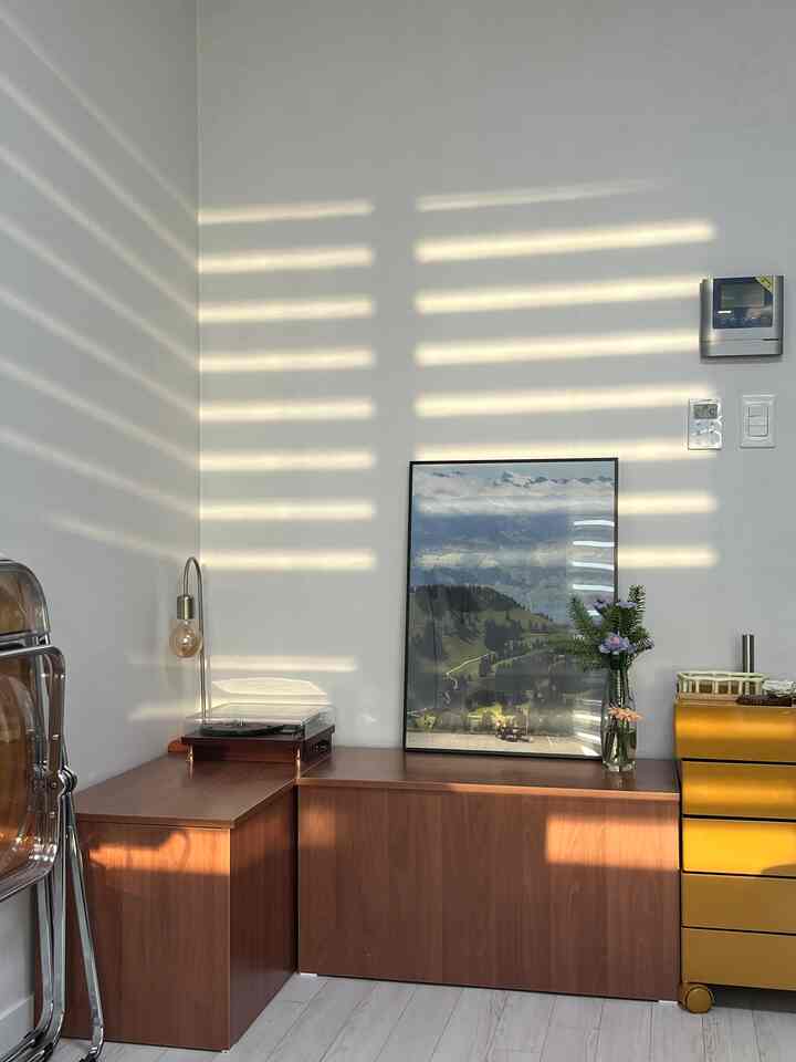 ナチュラルカラーのリビングコーナー、木製キャビネットとポスター、ヴィンテージの壁照明が配置された雰囲気のあるインテリア