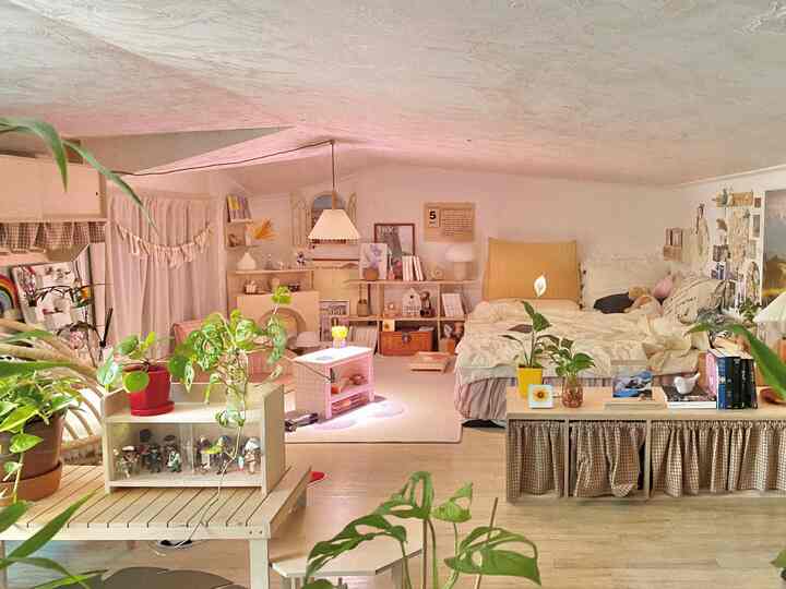 White and beige toned bedroom featuring multiple plants, storage areas, and cozy bedding with cushions