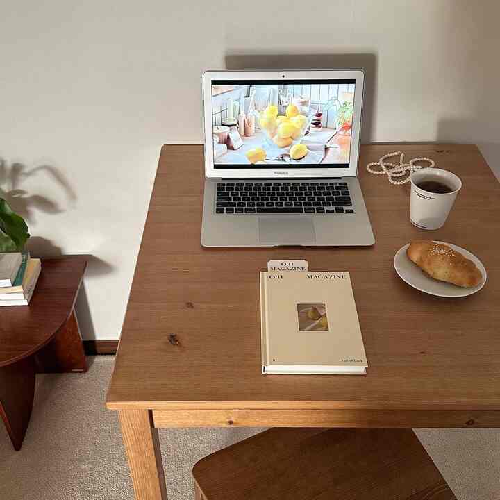 Beige-walled, wood-tone dining table simple remote work space with books, laptop, and coffee