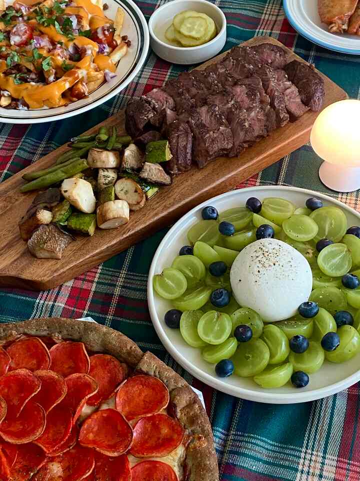 Cozy dining table with red and green tone plaid tablecloth featuring various Christmas home party dishes and plating