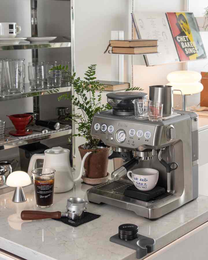 Silver and white toned kitchen counter featuring a coffee machine, coffee cups, and a plant in a home cafe setting