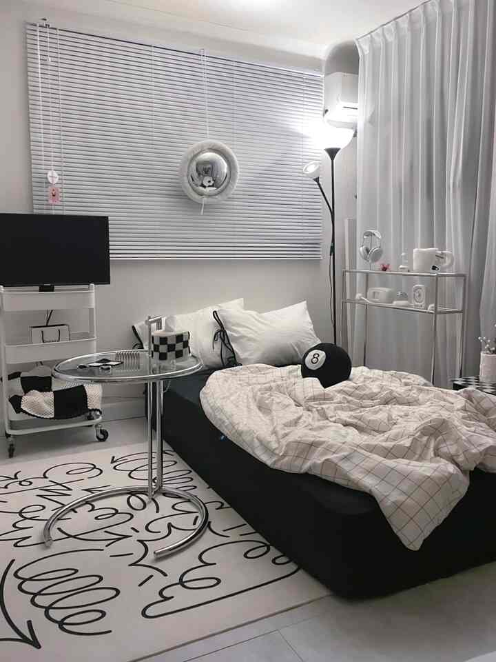 モダンな白黒トーンの寝室、中央にシングルベッドとサイドテーブル、大きなブラインドとカーテンが配置された落ち着いた空間