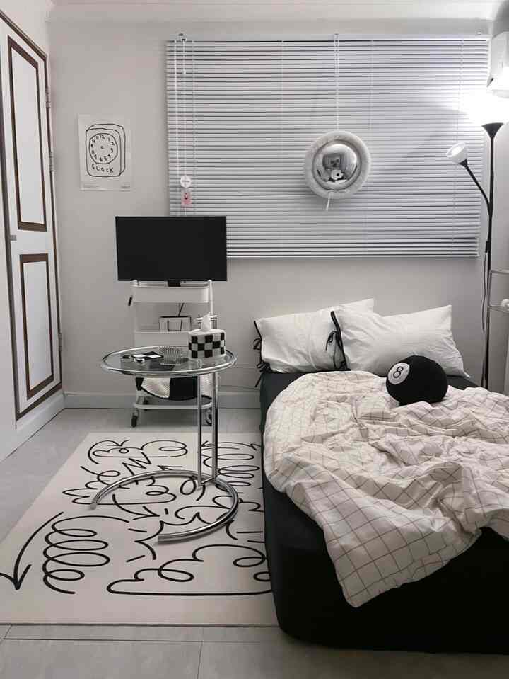 白と黒のトーンのワンルーム寝室、ベッドとメタリックサイドテーブル、ブラインドが配置されたモダンなインテリア