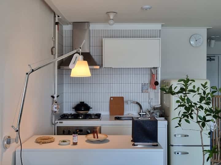 White and natural toned kitchen featuring wall-mounted lamp and vintage refrigerator with a clean and cozy atmosphere