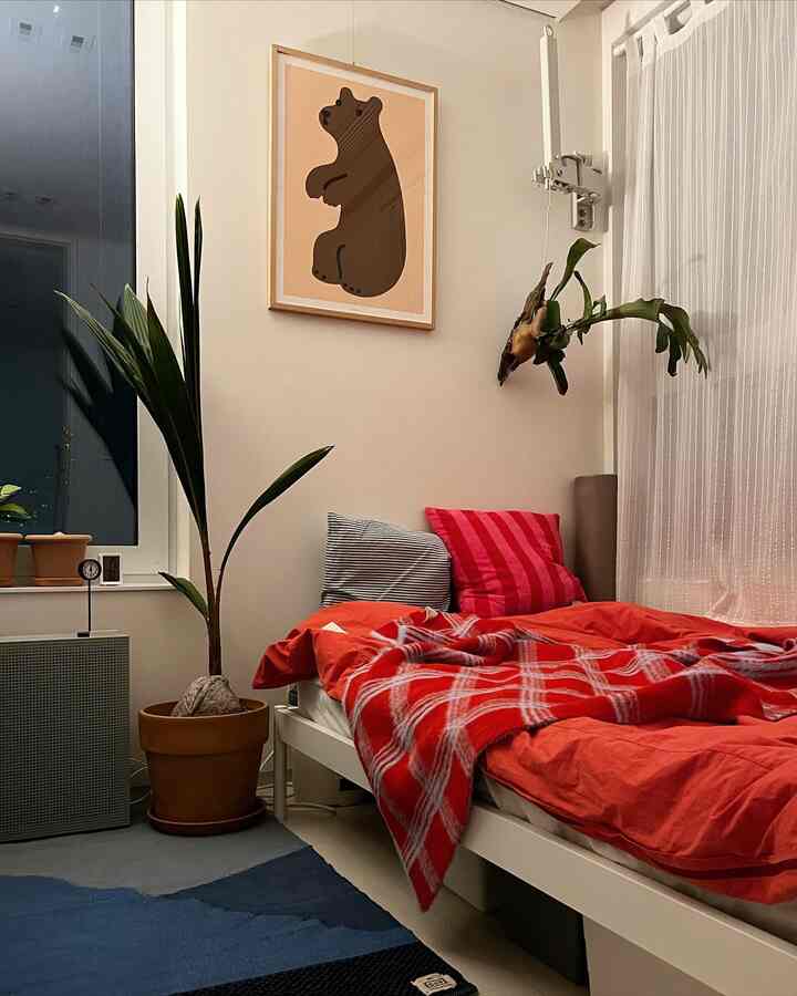 白い壁と赤い寝具が調和した居心地の良い寝室、テラコッタ鉢と植物が自然で温かみのある雰囲気を演出