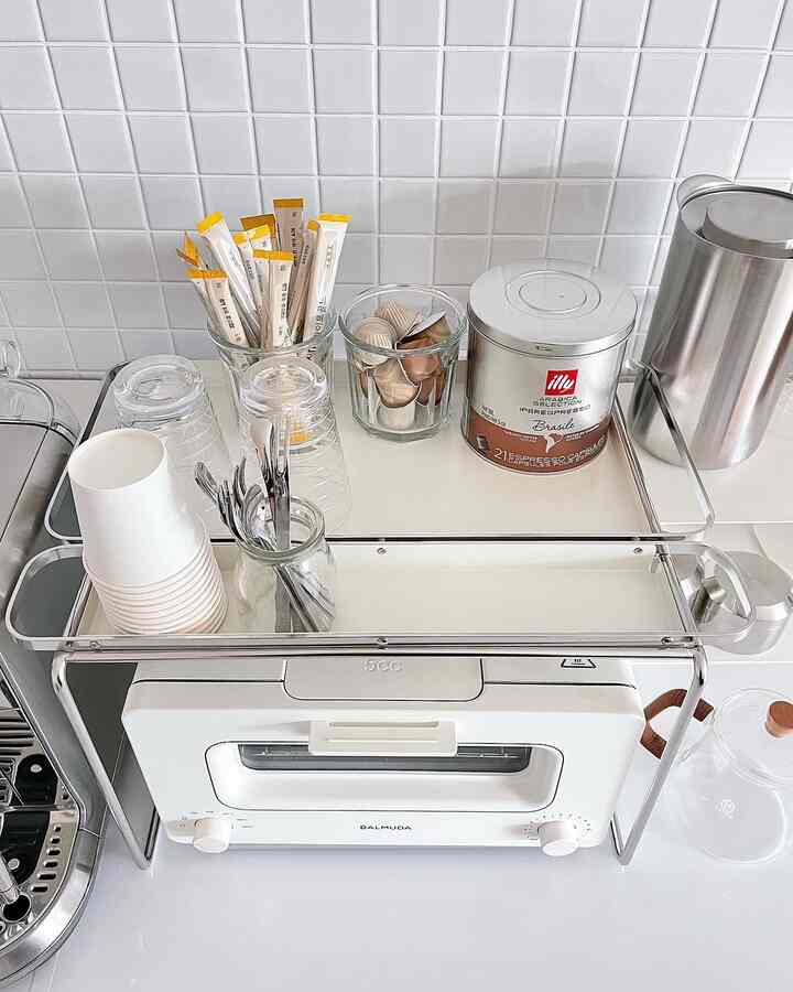 White tiled kitchen space featuring a neat home cafe setup with coffee capsules, cups, and a toaster rack organizing the countertop
