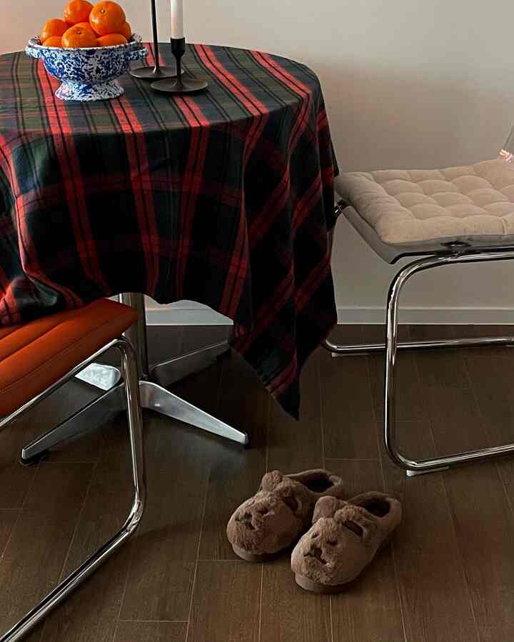 茶色と赤のトーンのダイニングルーム、円形のテーブルにチェック柄のテーブルクロスとファースリッパが配置された雰囲気のあるインテリア
