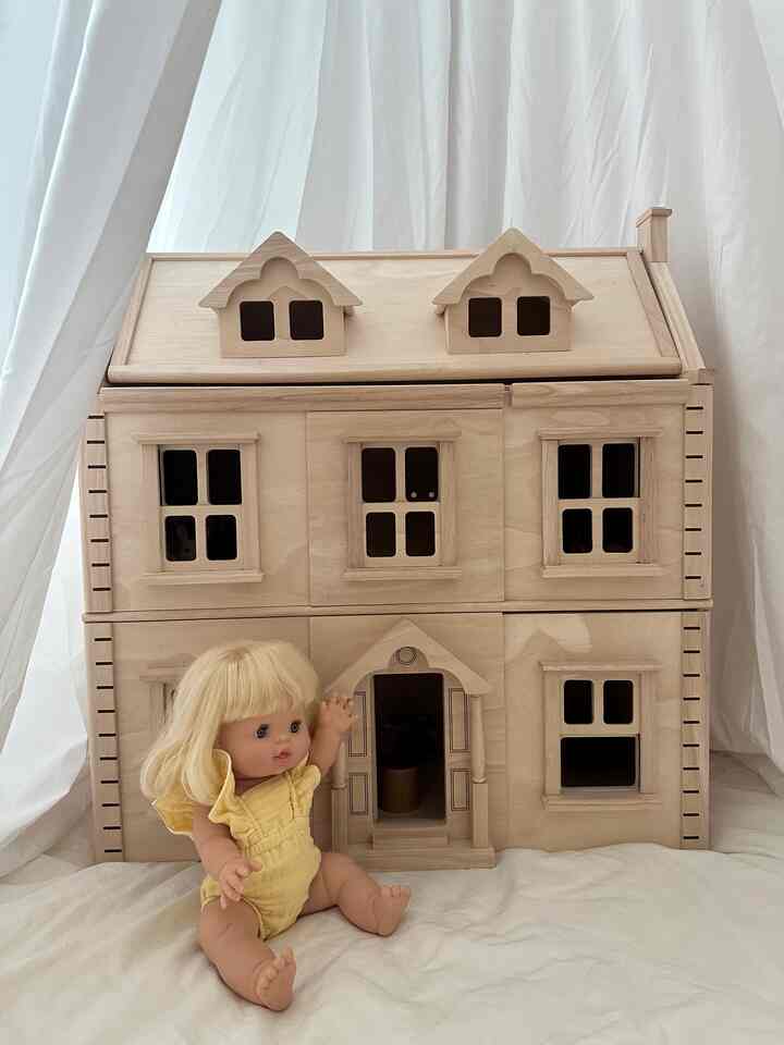 明るい木目調と白いカーテンを背景に、黄色い服を着た赤ちゃん人形が座っているドールハウスの風景