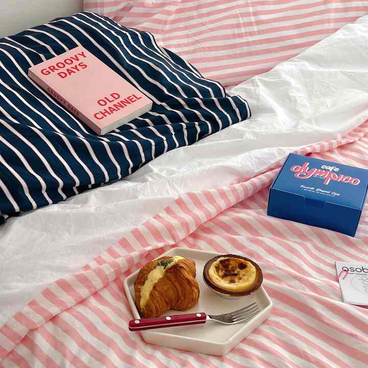 Pink and navy striped bedding in a bedroom featuring a plate with cake and croissant and cutlery, creating a cozy atmosphere
