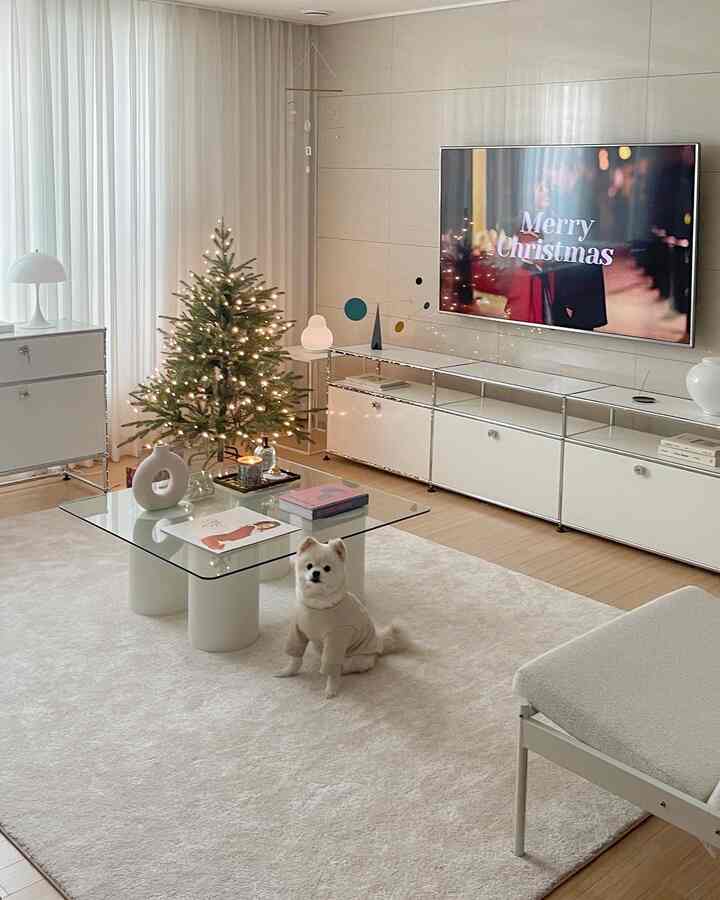 白と木目調の調和したモダンなリビング、中央にガラスのテーブルとクリスマスツリーが配置された暖かな空間