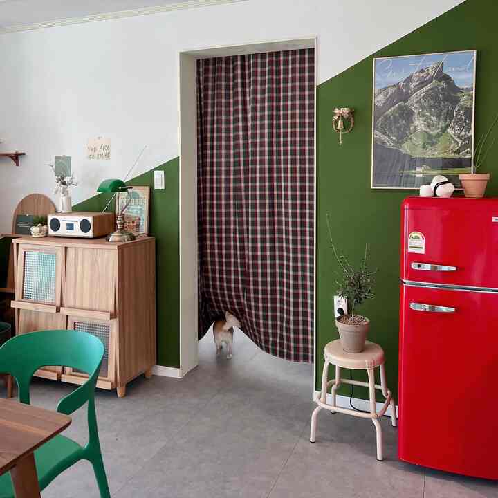 Office interior with green walls and a red mini retro refrigerator, featuring wood storage cabinet and plaid curtain for a cozy vibe