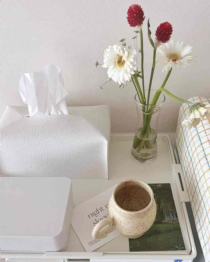 白を基調としたワンルームのテーブルに、ベージュのカップと透明な花瓶が置かれた雰囲気のあるインテリア