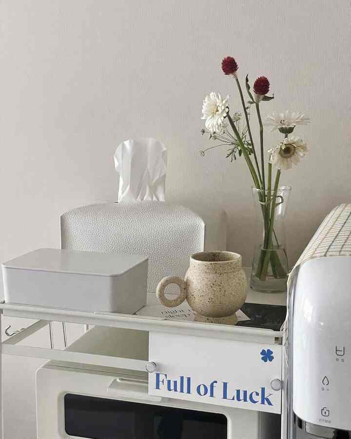 White-toned kitchen space featuring a vase and cup on a neat, minimal tabletop with small appliances