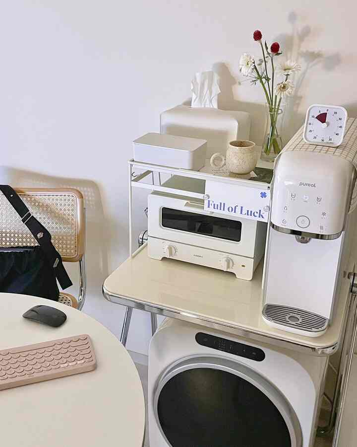 White-toned small kitchen space featuring a toaster rack, cold and hot water purifier, and round dining table in a neat home cafe setup