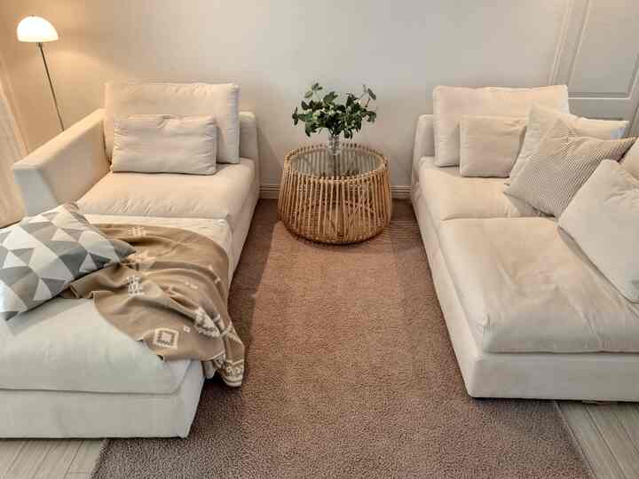 A white and beige toned living room featuring two sofas and a round rattan coffee table, creating a cozy natural home cafe atmosphere