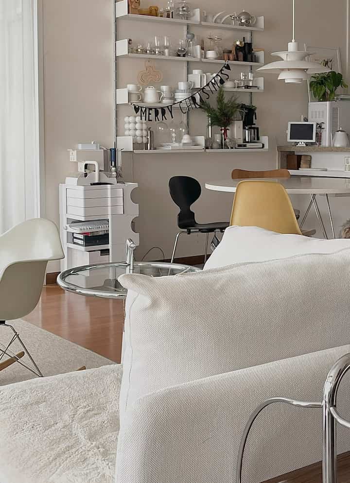 White and brown toned kitchen space featuring a round dining table, assorted chairs, wall shelves with garland decoration, presenting a cozy cafe-style interior