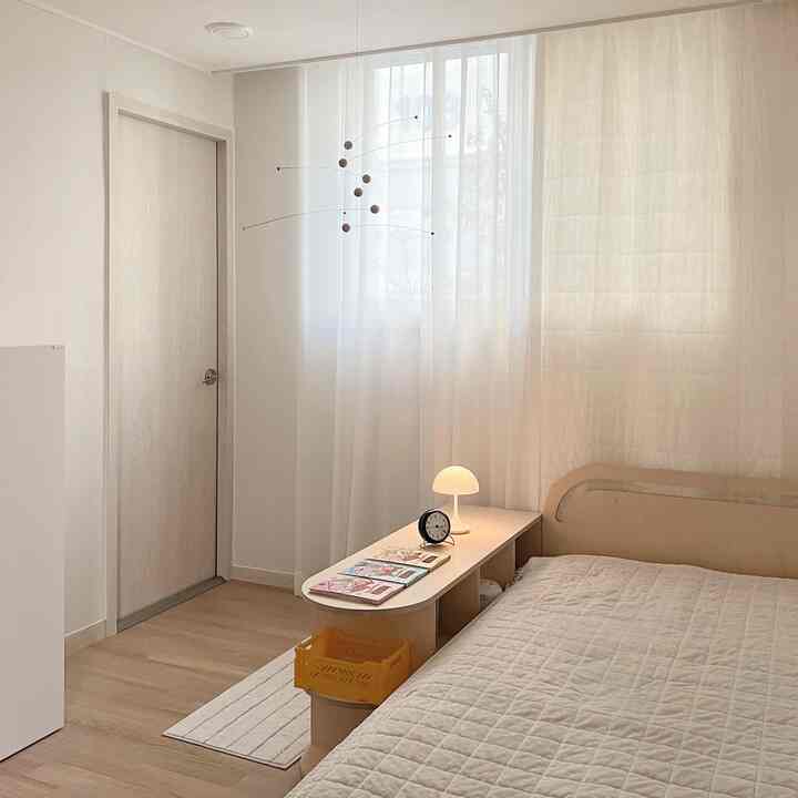 ホワイトとベージュの色調の子供部屋、モビールとベッド、カーテンが配置された暖かく落ち着いたインテリア