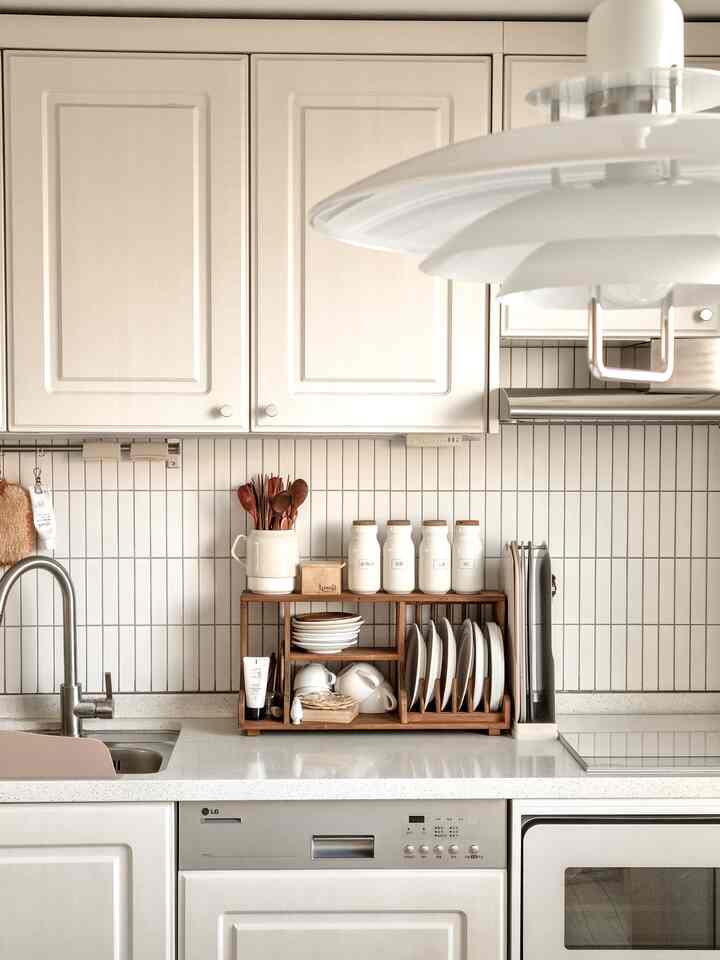 A white and wood tone kitchen featuring a dish rack with plates and spice jars neatly arranged
