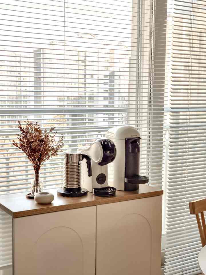 ホワイトと木目調が調和したキッチンのおうちカフェ空間、コンパクトな収納キャビネットとコーヒーマシンが配置された温かみのあるインテリア