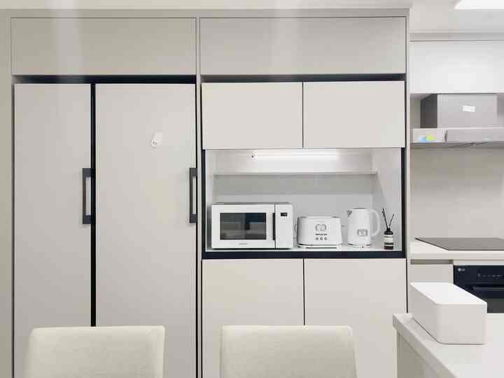 A simple kitchen space in Cota White and Smoky Gray tones, featuring bespoke refrigerator cabinets and microwave with a clean aesthetic