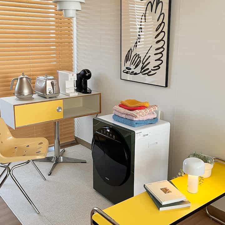 Minimal and modern kitchen space in yellow and white tones featuring a compact dryer and coffee machine