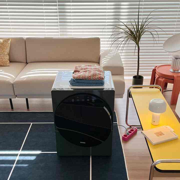 White and navy toned living room featuring beige sofa, yellow bench, compact dryer, and table lamp in a modern clean space