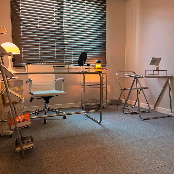 グレーのカーペットと白い家具が調和するモダンな書斎、透明な椅子と暖かな照明があるコンパクトなレイアウト