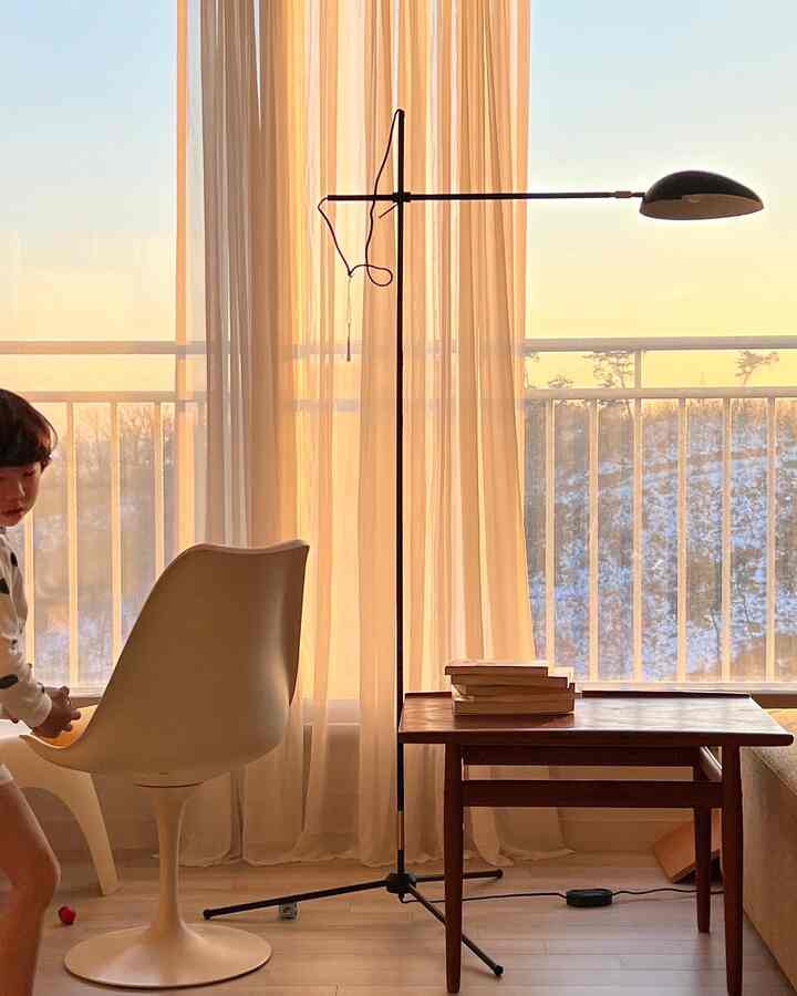 Warm natural-toned living room with large windows and curtains, wooden table and floor lamp creating a cozy space