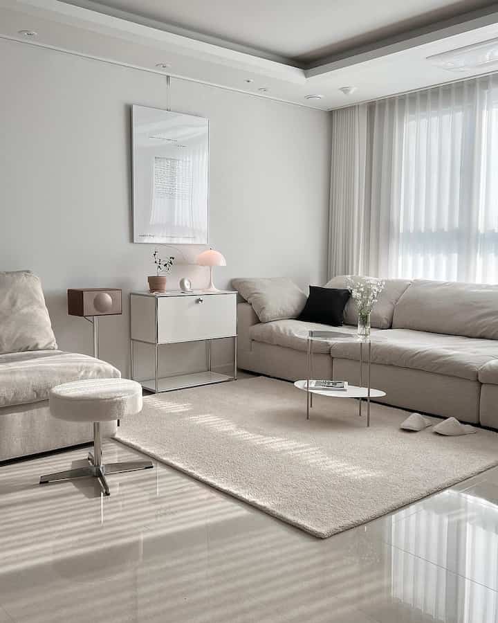 Bright white and beige toned living room featuring fabric sofas, transparent coffee table, and rug, creating cozy natural atmosphere