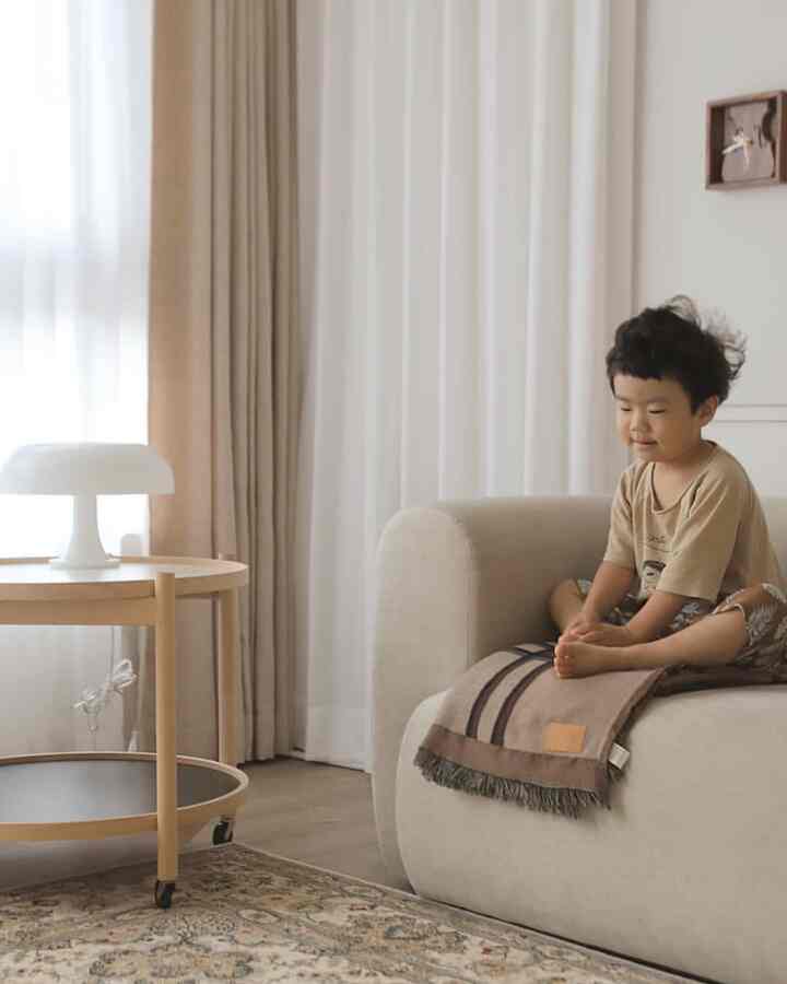 Beige and natural wood-toned living room featuring a sofa and side table with a child sitting comfortably, creating a cozy atmosphere