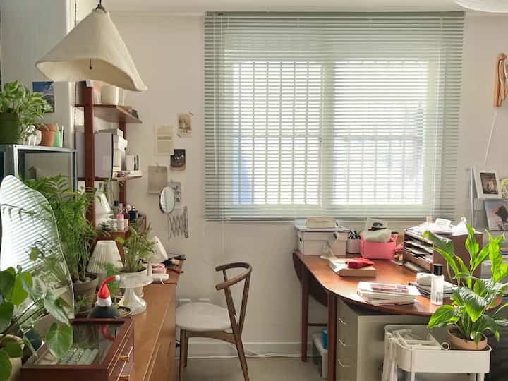Cozy home office with white walls, brown wooden furniture, a desk, aluminum blinds, and multiple green plants