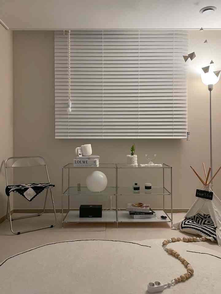 Beige and white toned living room featuring central white blinds, metal folding chair on left, pet tent and toys on right floor creating cozy ambiance