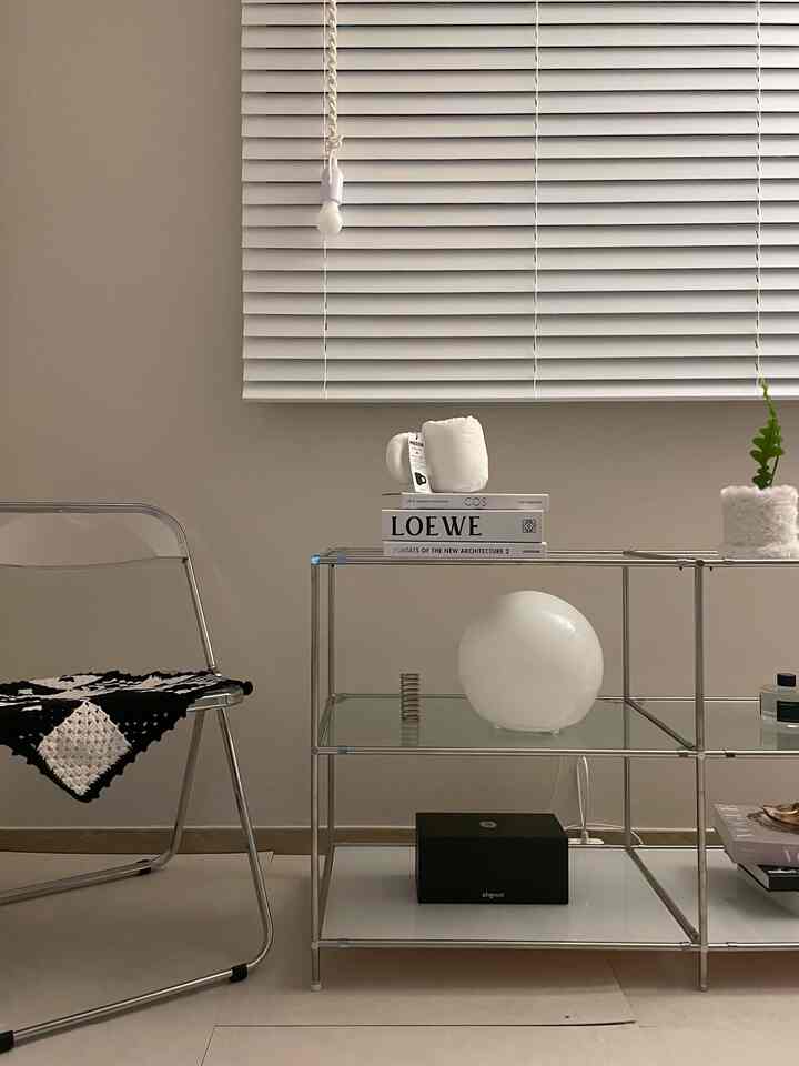Minimal living room in white, silver, and transparent tones featuring metal shelves and a clear chair with clean design