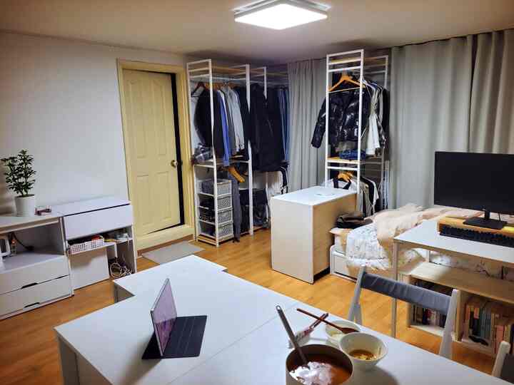 Modern home office interior for a single household featuring white and wood tones with combined compact walk-in closet and bedroom space