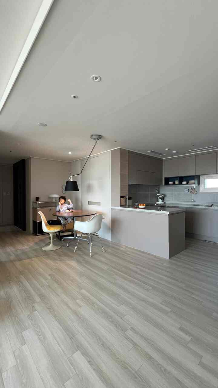 Bright wood-tone flooring and white walls blend in a mid-century modern kitchen and dining room featuring a child seated on dining chair
