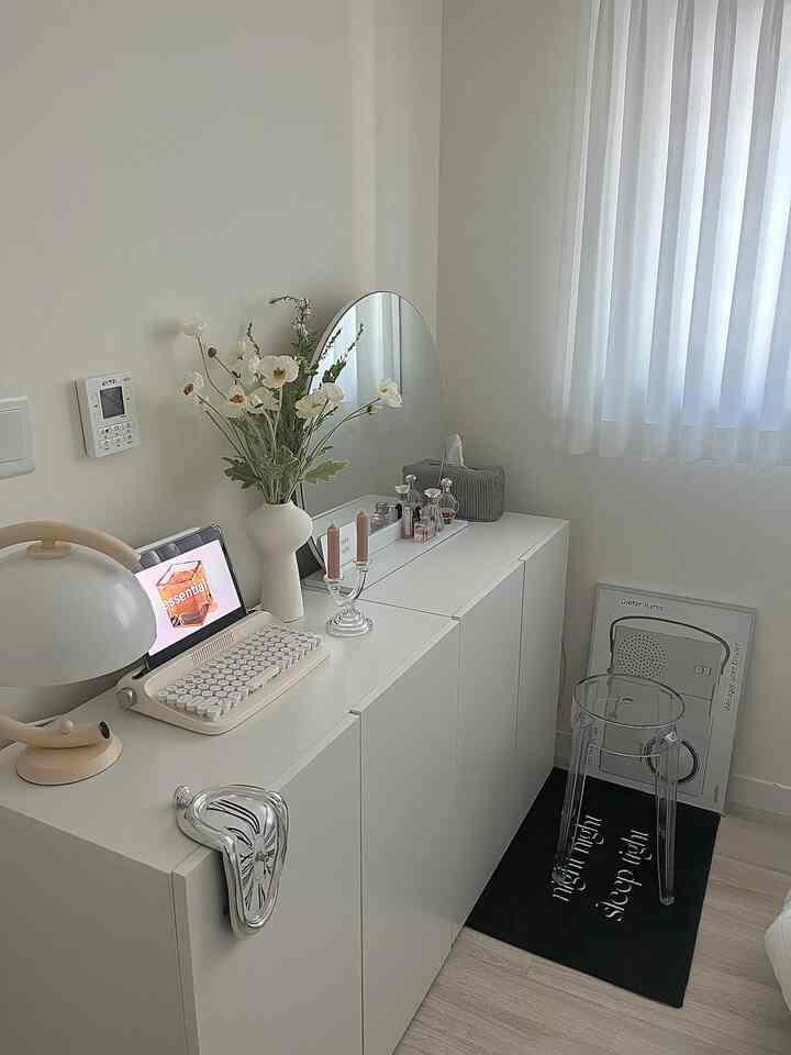White-toned bedroom space featuring a white vanity with oval mirror and a transparent acrylic stool, creating a simple and natural atmosphere