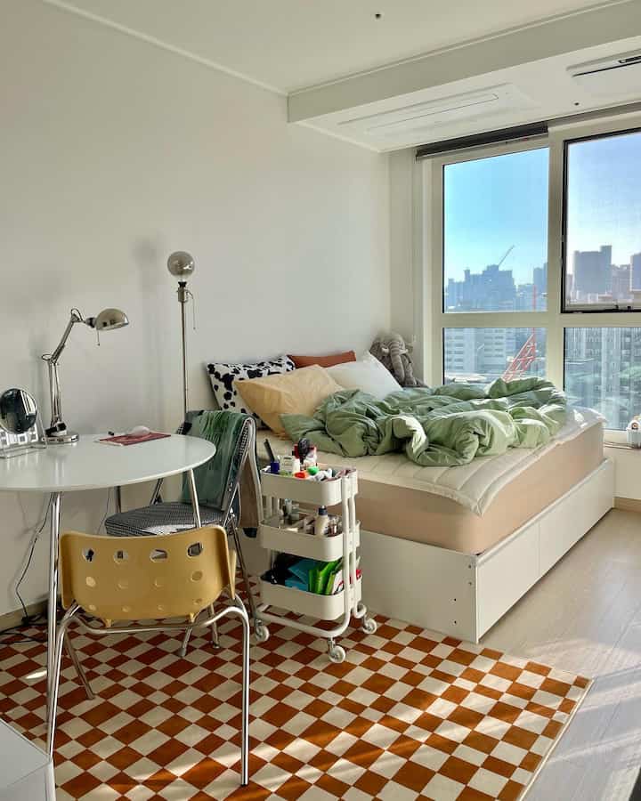 Natural modern compact bedroom with white walls, round table, and storage bed illuminated by bright natural light