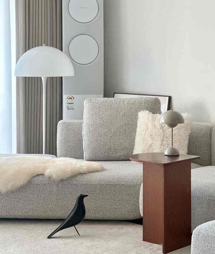 Bright beige and gray toned living room featuring a gray sofa, wooden side table, and floor lamp in a simple modern setting
