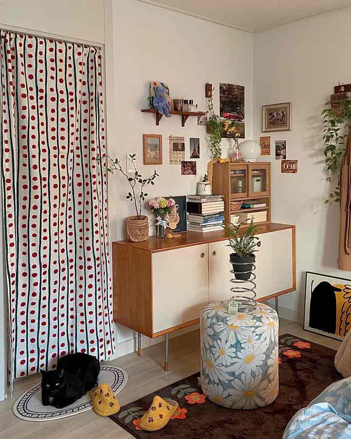 Bedroom with red polka dot curtain, wooden storage cabinet, plants, and floral stool in a vintage style interior