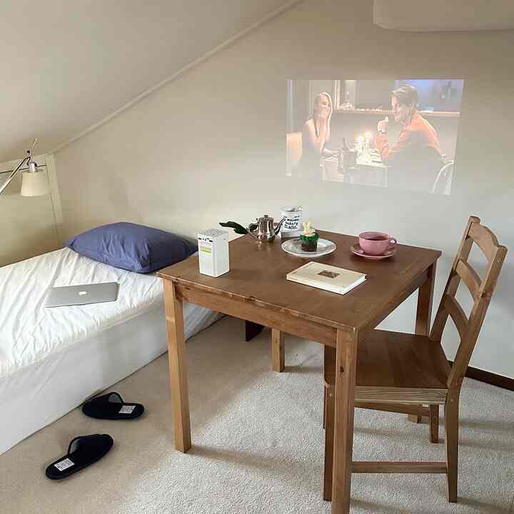 White and wood tone loft bedroom featuring a wooden dining table and chair with a mini projector and home cafe elements in a cozy setting