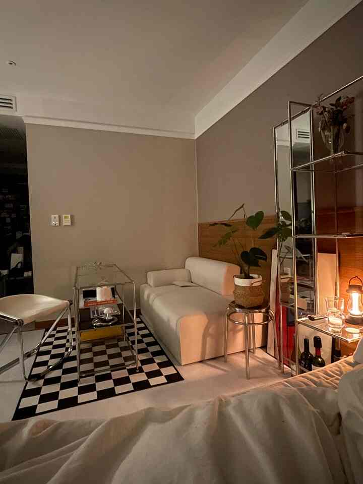 White and black toned mid-century modern studio apartment featuring a compact sofa, checkerboard rug, and modular shelving in a cozy atmosphere
