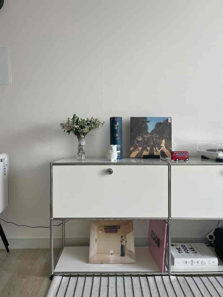White-toned living room featuring a minimalist white sideboard with vase and vintage decor elements creating a modern retro atmosphere