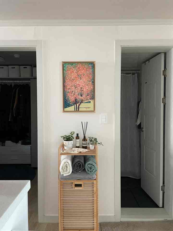 White and beige toned wall space featuring a wooden storage rack decorated with diffusers and plants, presenting a clean natural atmosphere